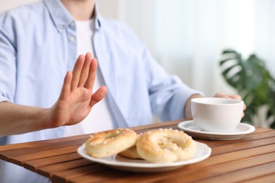 Photo of Gluten free diet. Man with cup of drink refusing from pastries at wooden table indoors, closeup