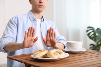 Photo of Gluten free diet. Man refusing from pastries at wooden table indoors, closeup