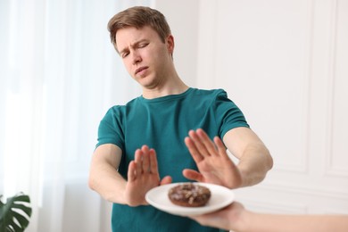 Photo of Gluten free diet. Man refusing from donut indoors, selective focus