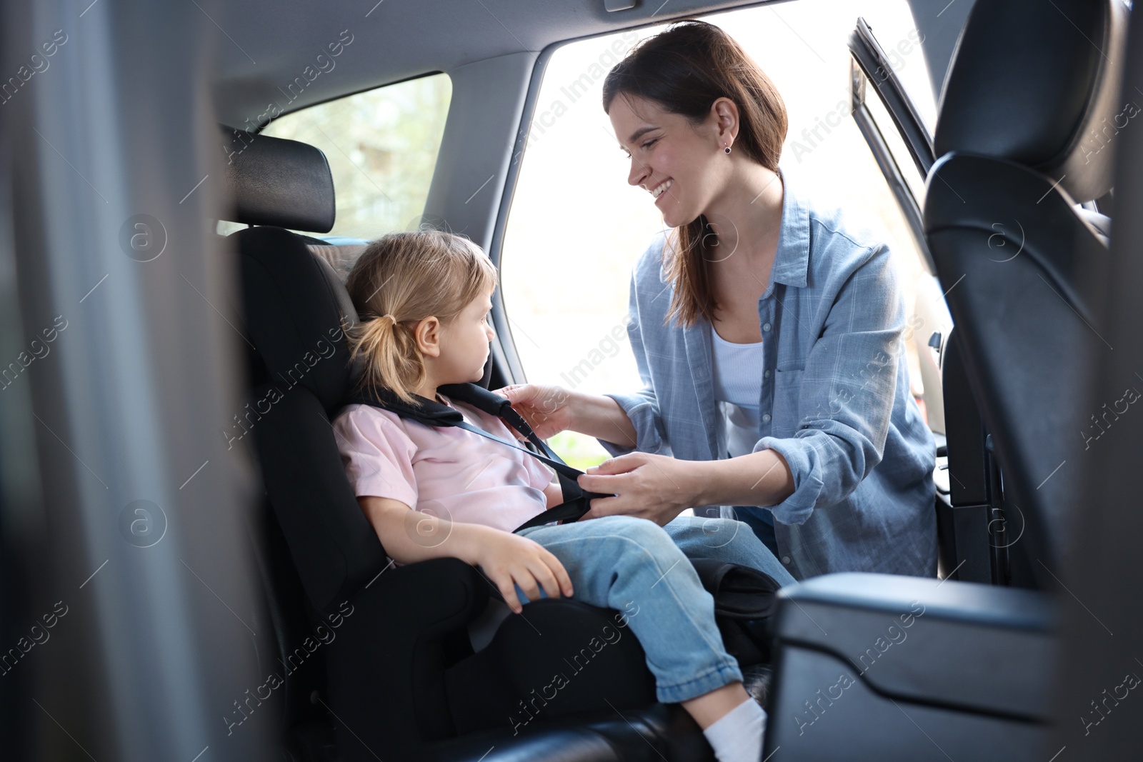 Happy mother fastening her daughter in child safety seat inside car Photo of Happy mother fastening her daughter in child safety seat inside car