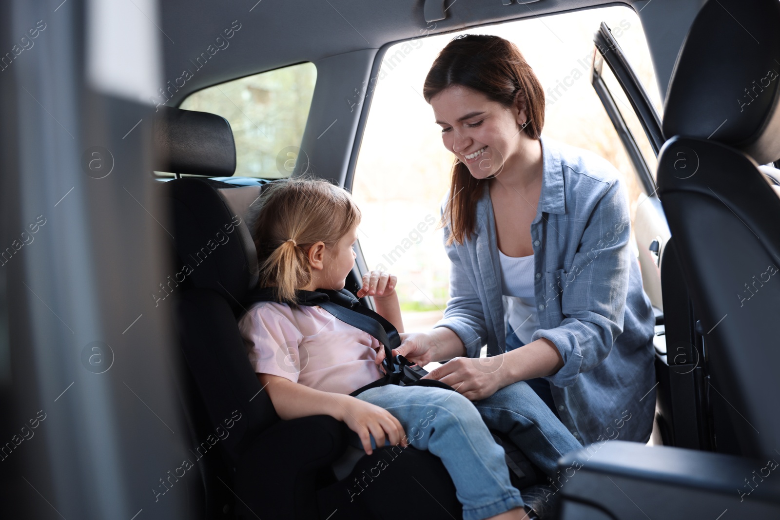 Happy mother fastening her daughter in child safety seat inside car Photo of Happy mother fastening her daughter in child safety seat inside car