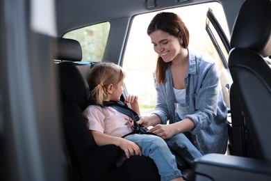 Photo of Happy mother fastening her daughter in child safety seat inside car