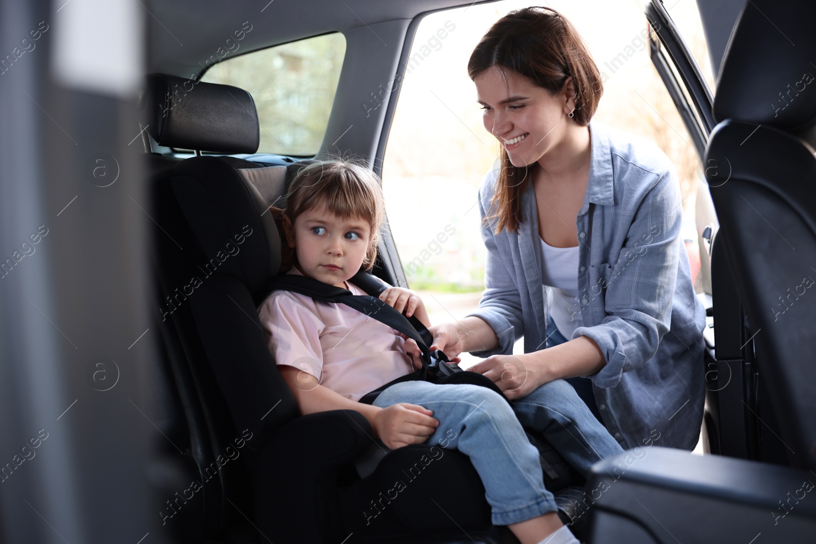 Happy mother fastening her daughter in child safety seat inside car Photo of Happy mother fastening her daughter in child safety seat inside car