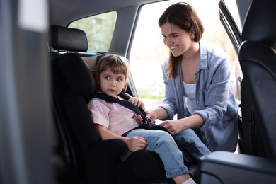 Photo of Happy mother fastening her daughter in child safety seat inside car