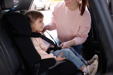 Photo of Mother fastening her daughter in child safety seat inside car, closeup