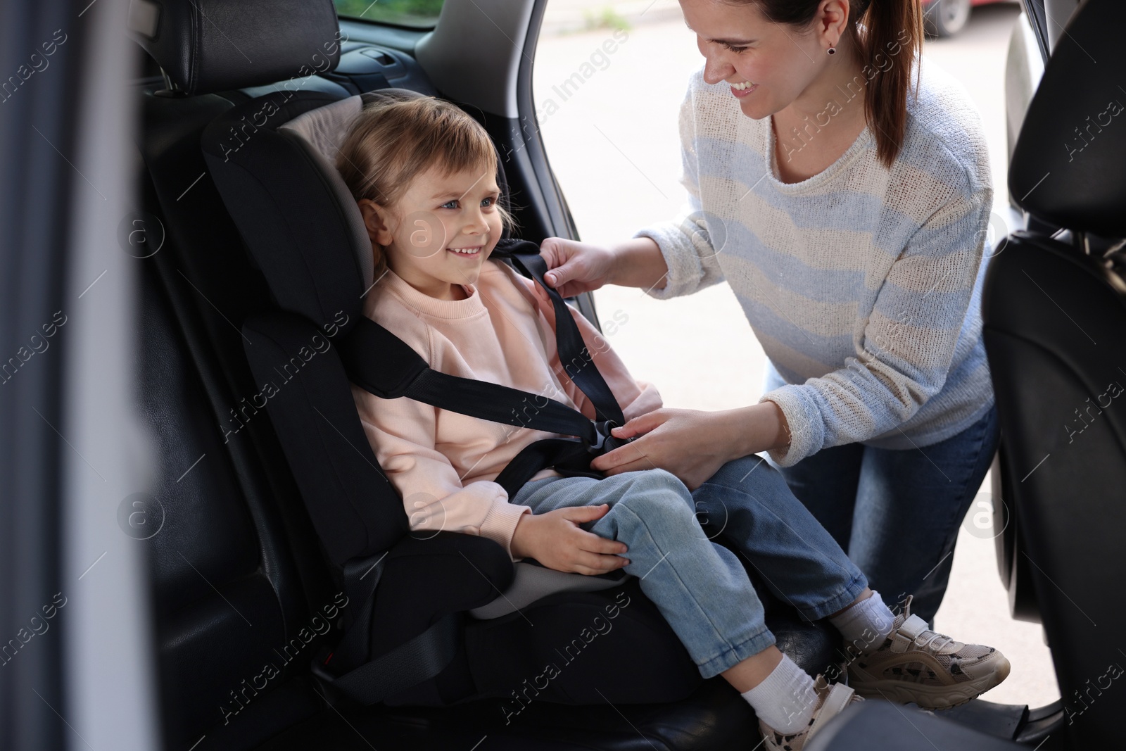 Happy mother fastening her daughter in child safety seat inside car Photo of Happy mother fastening her daughter in child safety seat inside car