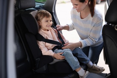 Photo of Happy mother fastening her daughter in child safety seat inside car