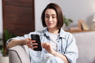 Photo of Woman using modern smartphone in armchair at home