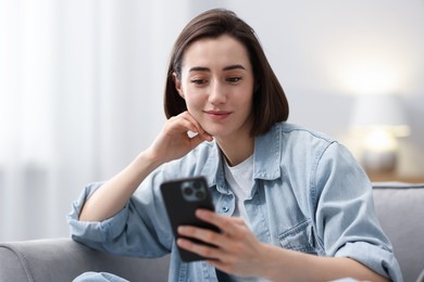 Photo of Woman using modern smartphone in armchair at home