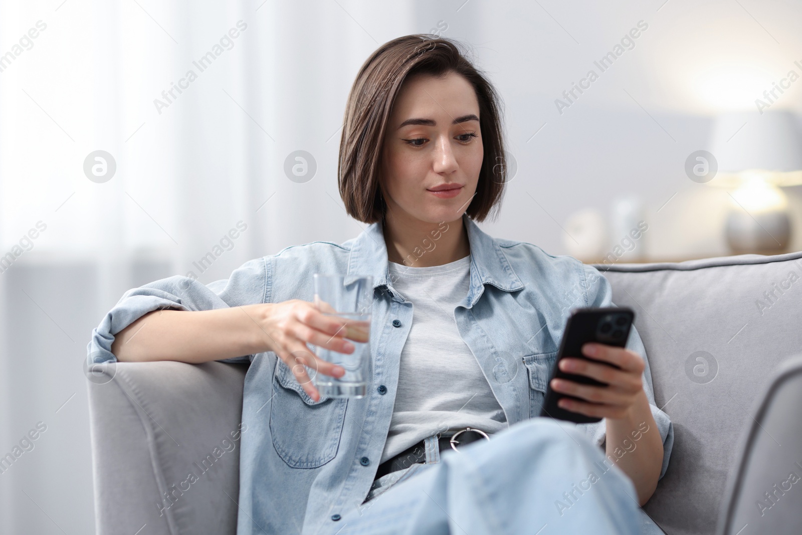 Woman using modern smartphone in armchair at home Photo of Woman using modern smartphone in armchair at home
