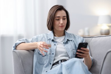 Photo of Woman using modern smartphone in armchair at home