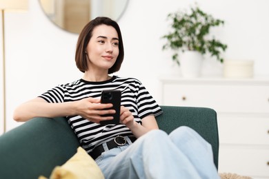 Photo of Woman using modern smartphone on sofa at home. Space for text
