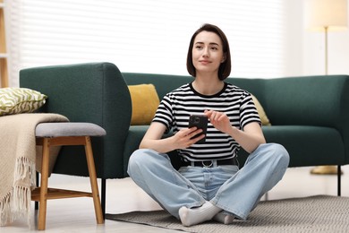 Photo of Woman using modern smartphone on floor at home