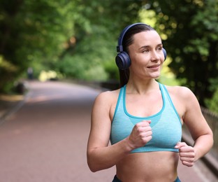 Photo of Sporty woman with headphones running in park, space for text