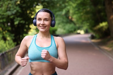 Photo of Sporty woman with headphones running in park, space for text