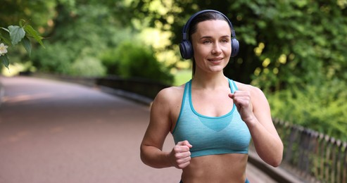 Photo of Sporty woman with headphones running in park, space for text
