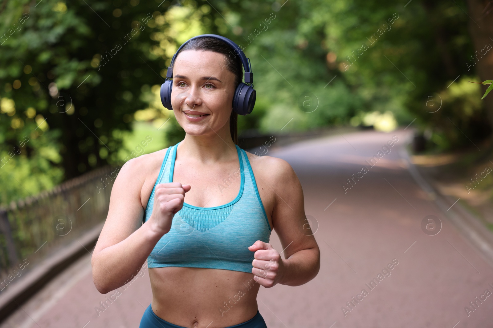 Sporty woman with headphones running in park, space for text Photo of Sporty woman with headphones running in park, space for text