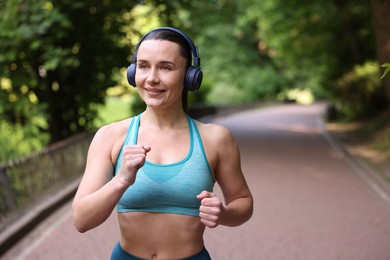 Photo of Sporty woman with headphones running in park, space for text