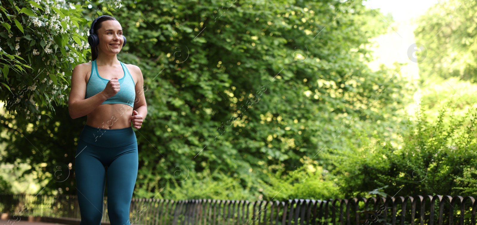 Sporty woman with headphones running in park, space for text Photo of Sporty woman with headphones running in park, space for text