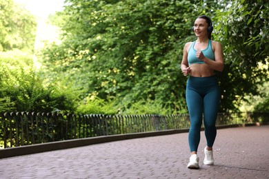 Photo of Sporty woman with headphones running in park, space for text