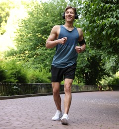 Photo of Sporty man with headphones running in park