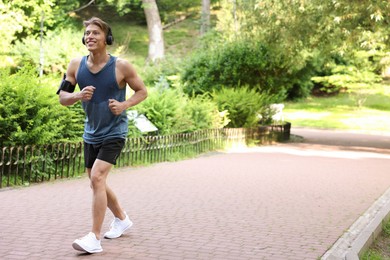 Photo of Sporty man with headphones running in park, space for text