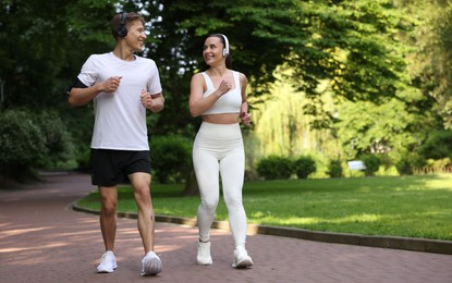 Photo of Sporty couple with headphones running in park, space for text
