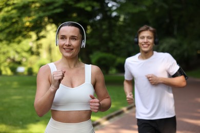 Photo of Sporty couple with headphones running in park, selective focus
