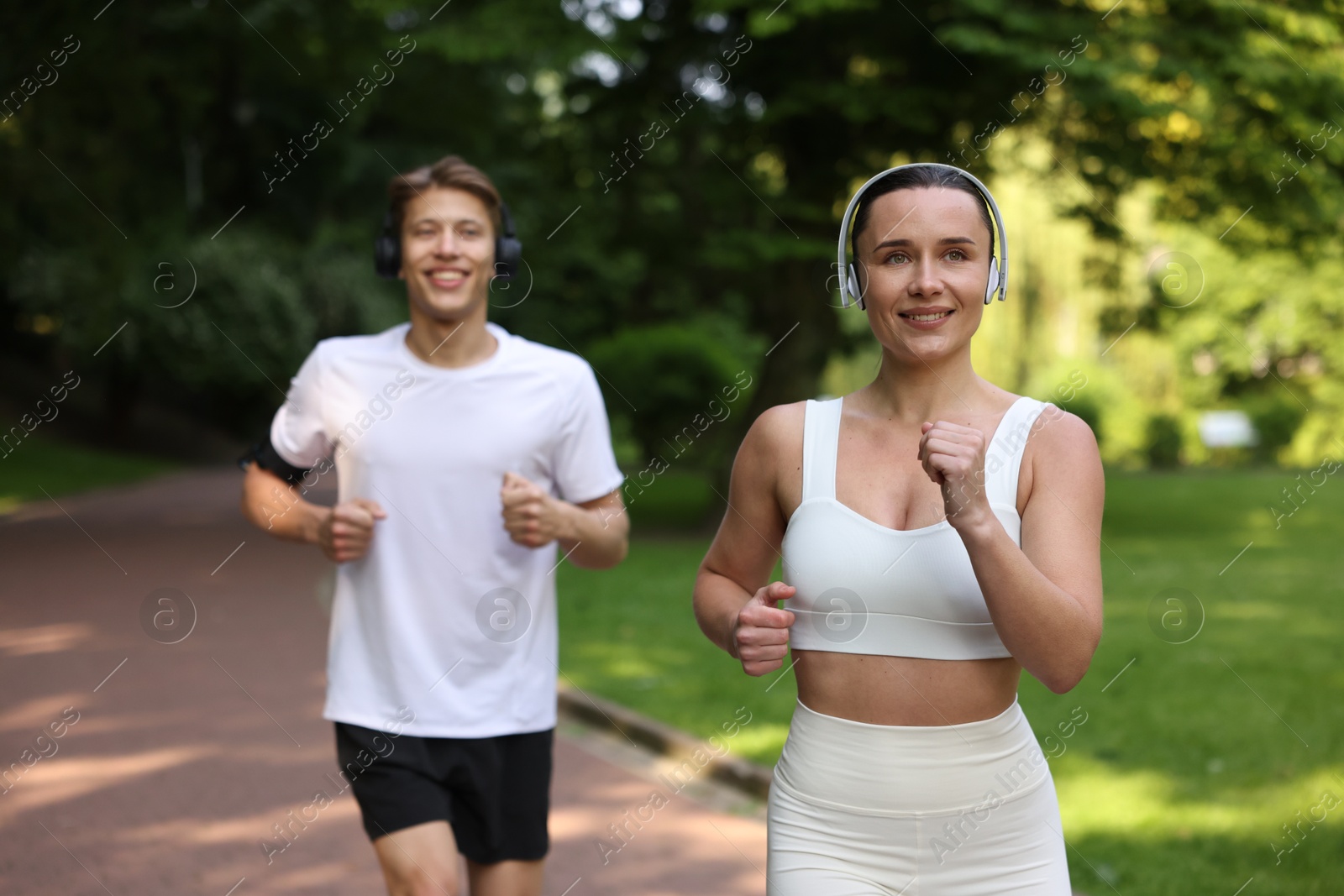 Sporty couple with headphones running in park, selective focus Photo of Sporty couple with headphones running in park, selective focus