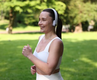 Photo of Sporty woman with headphones running in park