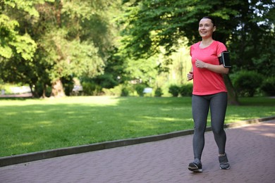 Photo of Sporty woman with armband running in park, space for text