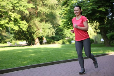 Photo of Sporty woman with armband running in park, space for text