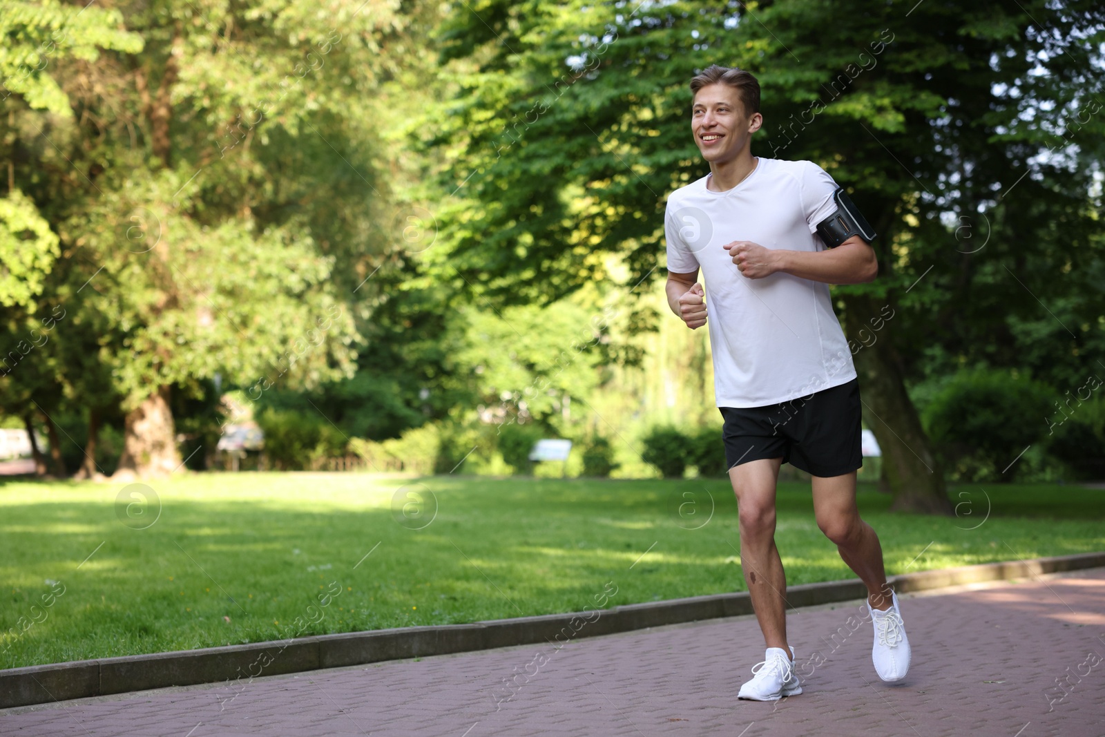 Sporty man with armband running in park, space for text Photo of Sporty man with armband running in park, space for text