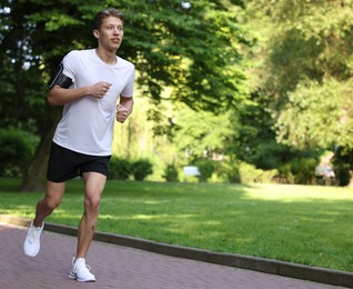 Photo of Sporty man with armband running in park, space for text