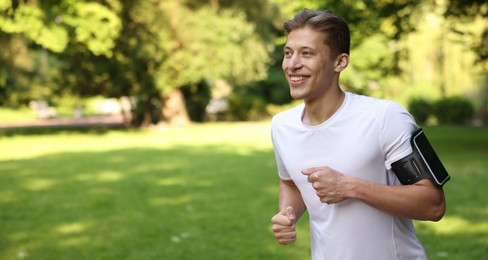 Photo of Sporty man with armband running in park, space for text