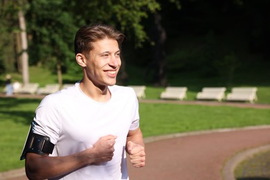 Photo of Sporty man with armband running in park, space for text