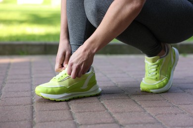 Photo of Woman tying shoelace of sneaker in park, closeup
