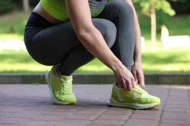 Photo of Woman tying shoelace of sneaker in park, closeup