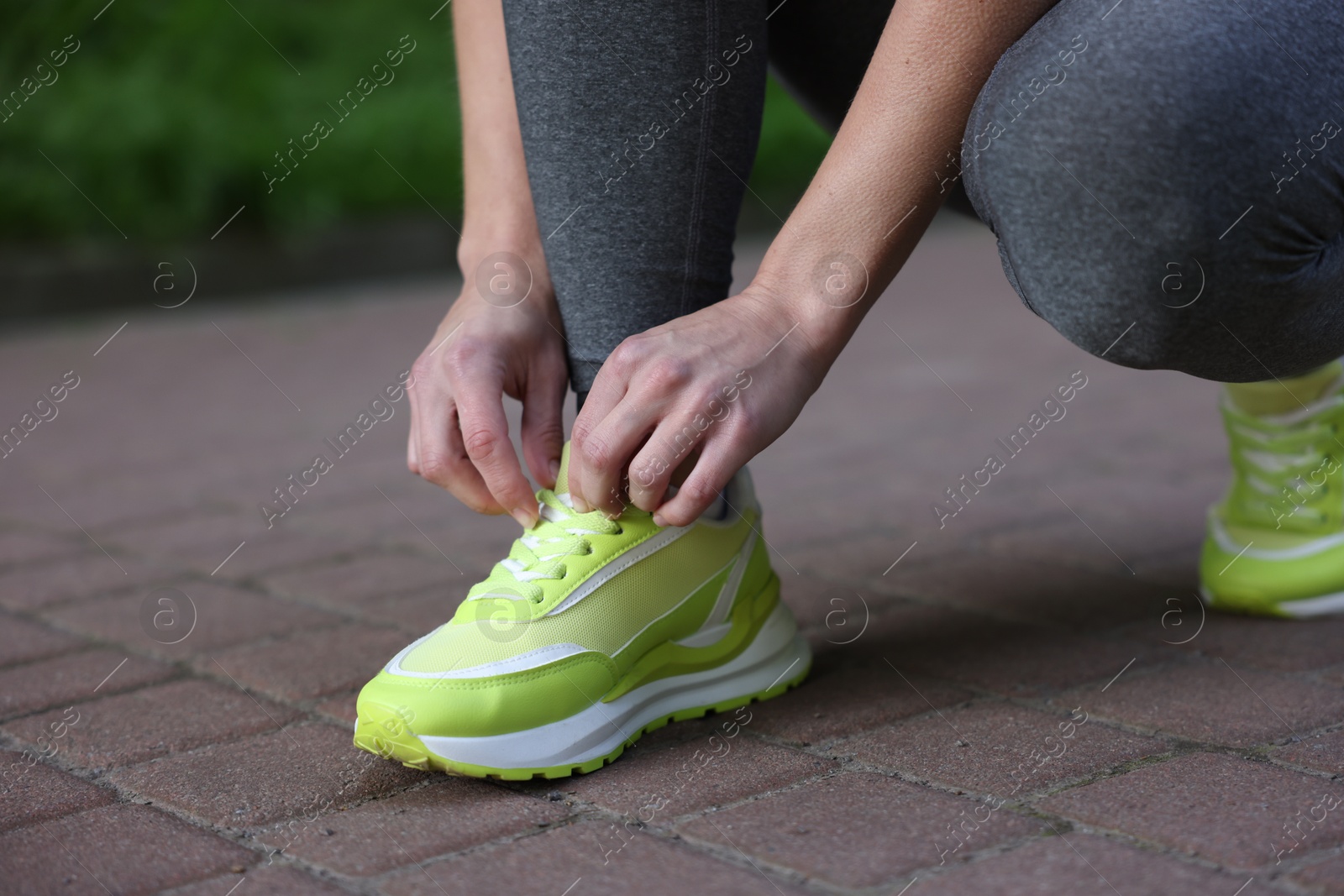 Woman tying shoelace of sneaker in park, closeup Photo of Woman tying shoelace of sneaker in park, closeup