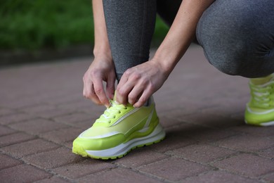 Photo of Woman tying shoelace of sneaker in park, closeup