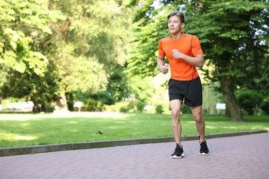 Photo of Sporty man running in park, space for text