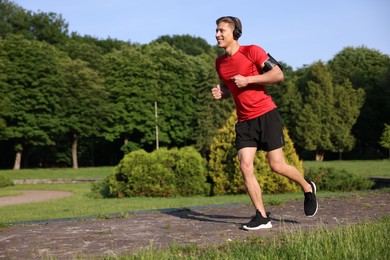 Photo of Sporty man with headphones running in park, space for text