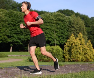 Photo of Sporty man with headphones running in park, space for text