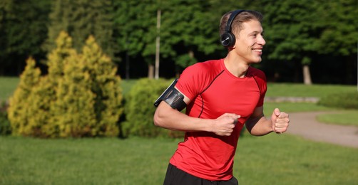 Photo of Sporty man with headphones running in park, space for text