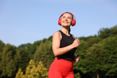 Photo of Sporty woman with headphones running in park, low angle view. Space for text