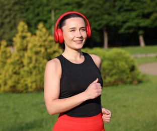 Photo of Sporty woman with headphones running in park