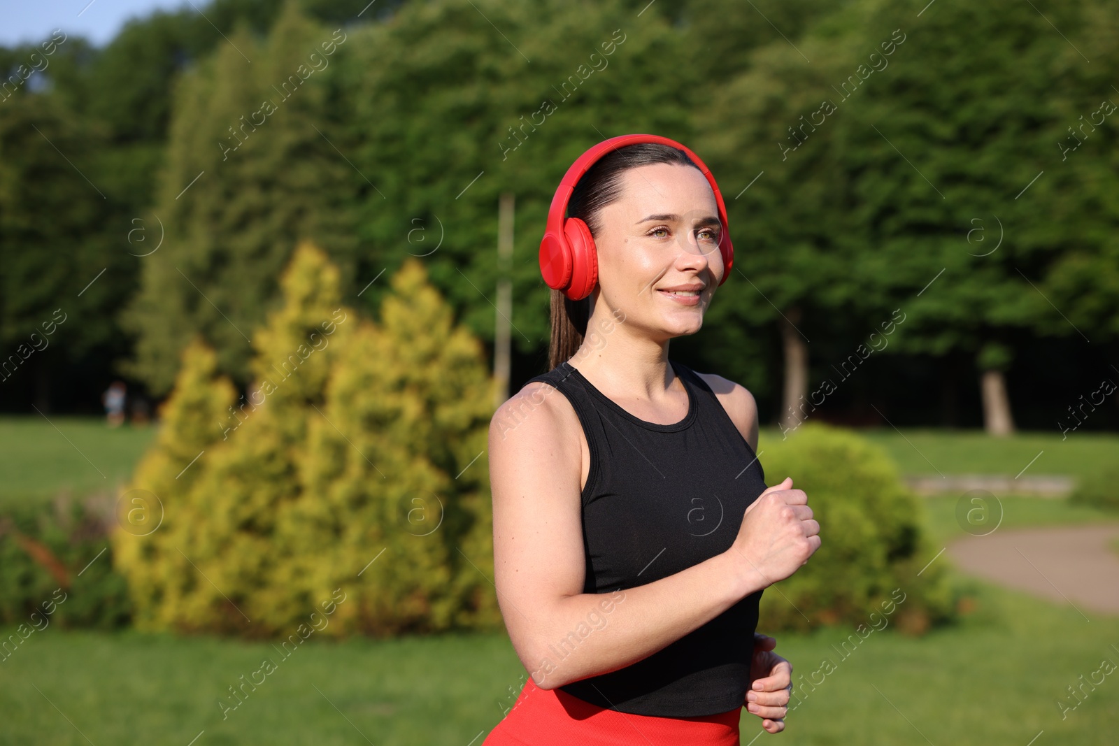 Sporty woman with headphones running in park, space for text Photo of Sporty woman with headphones running in park, space for text