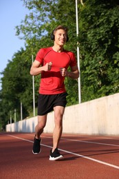 Photo of Sporty man with headphones running at stadium, low angle view
