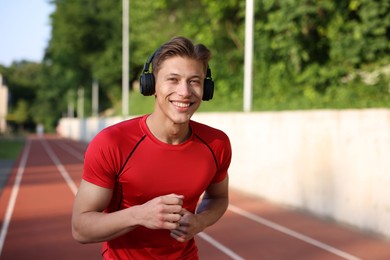 Photo of Sporty man with headphones running at stadium, space for text