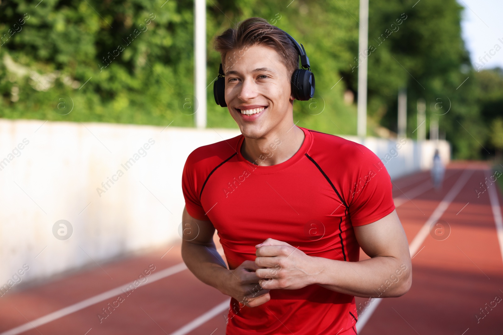 Sporty man with headphones running at stadium, space for text Photo of Sporty man with headphones running at stadium, space for text